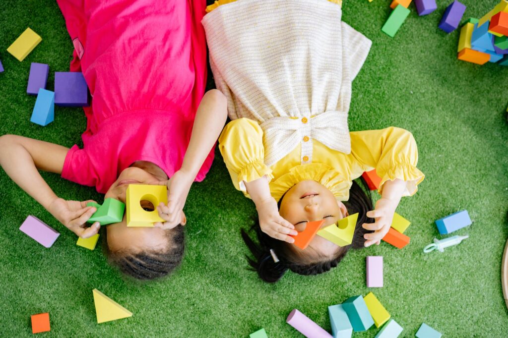 girls lying down on green carpet playing with wooden blocks